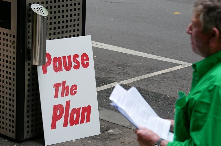 A sign reading pause the plan leans against a bin on a Melbourne street