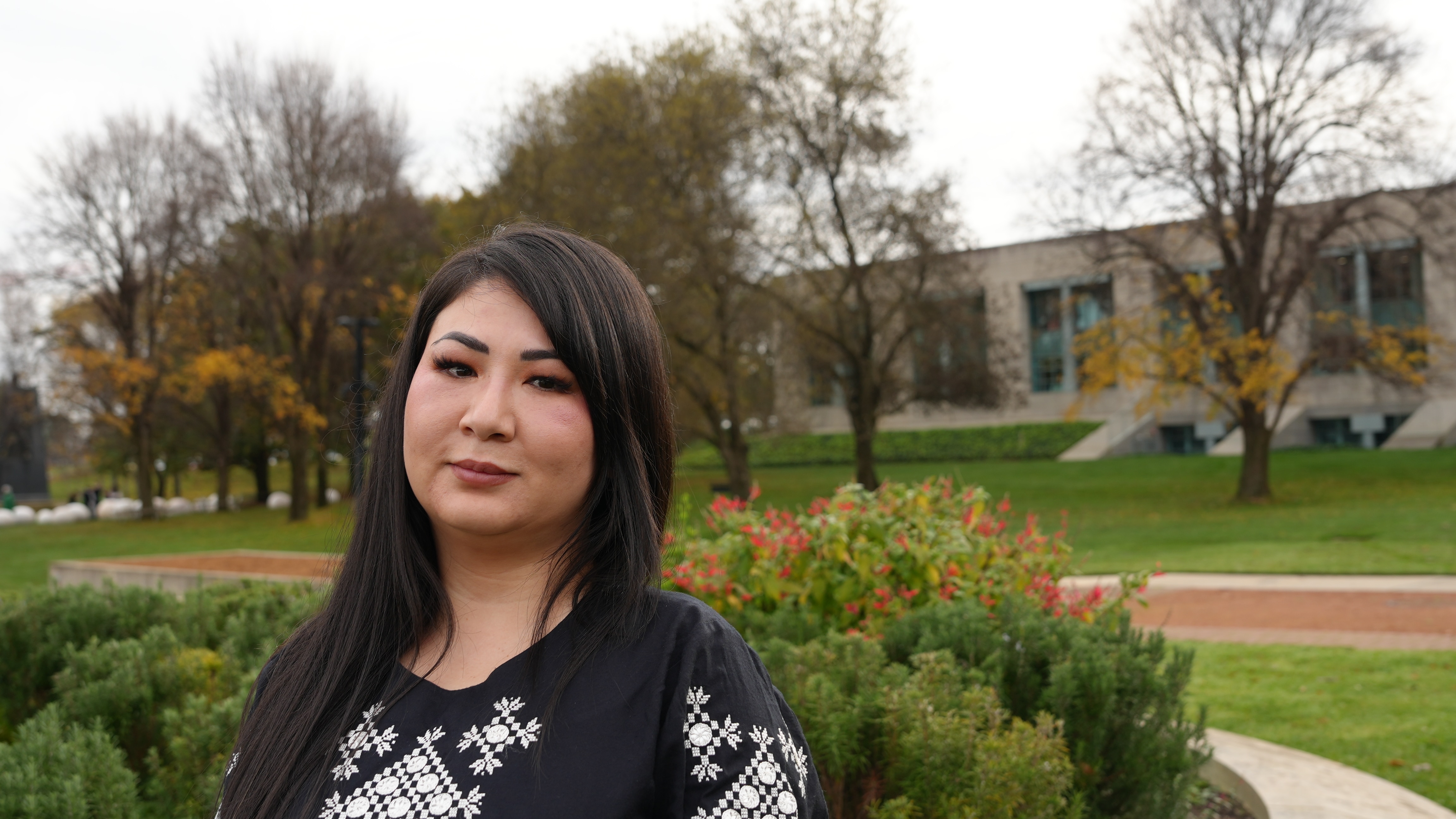 A woman with dark long hair stands outside smiling.