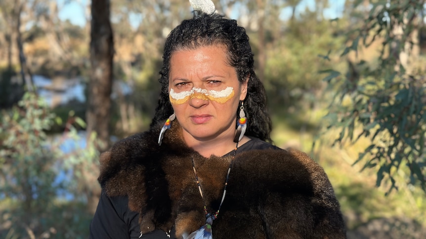 A lady wearing indigenous clothing frowns at a camera