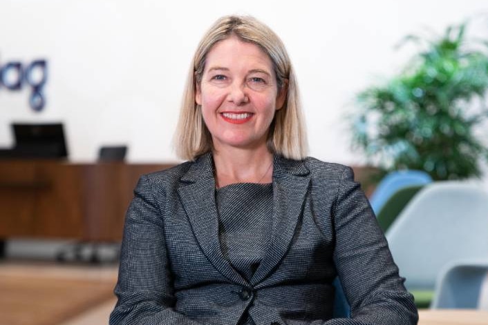 A woman in a grey suit smiling at the camera in an office.