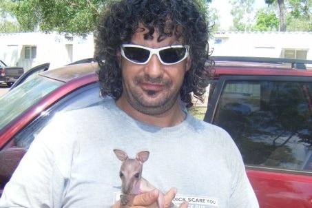 A man holds a kangaroo joey wearing sunglasses.