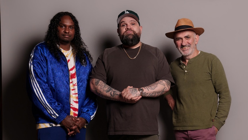 Baker Boy, Briggs and Paul Kelly pose against a grey photoscreen in a studio