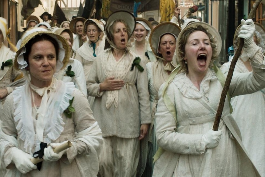 Colour still of a group of female demonstrators marching with flags and banners in 2018 film Peterloo.