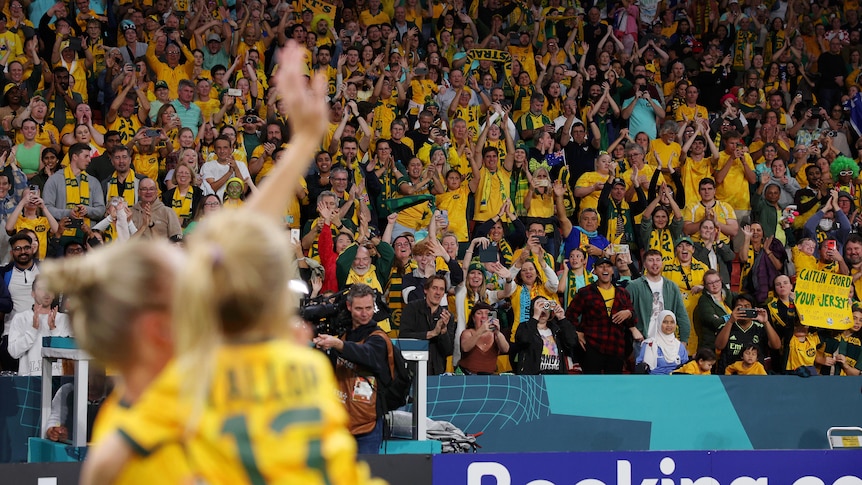 Tameka Yallop (blurry in the foreground) carries her daughter as she waves to an applauding crowd at the FIFA Women's World Cup.