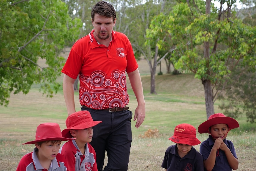 Principal Lachlan Moore in red school polo shirt, short brown hair, facial hair, four students in foreground.