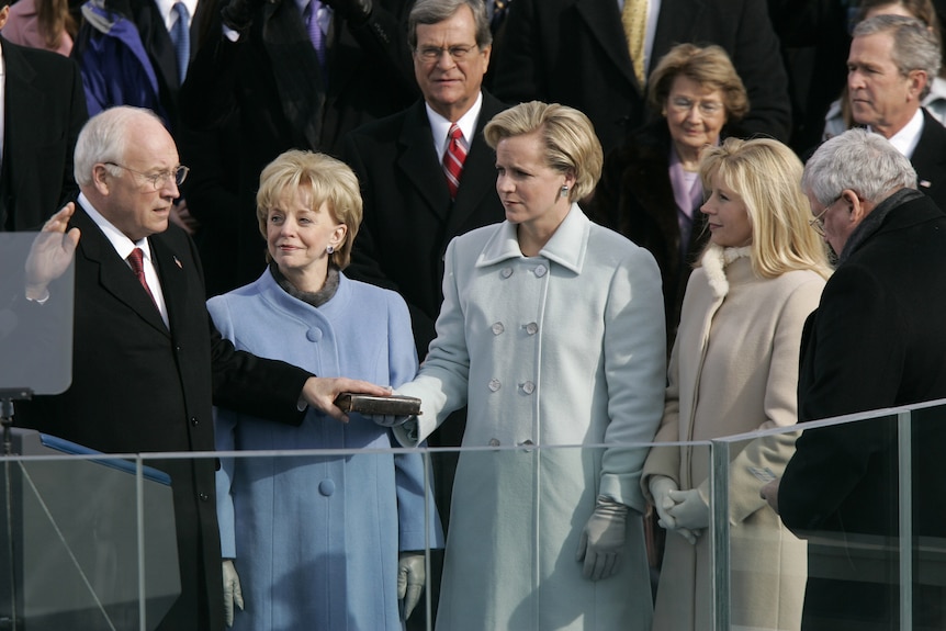 Dick Cheney holding one hand on a bible and one hand up as his wife and daughters look on