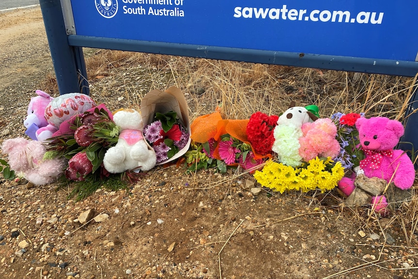 Flowers and teddy bears on the ground under a sign