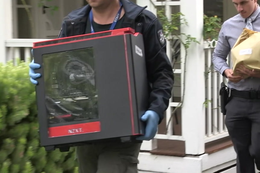 Police remove a piece of equipment from a house following a raid targeting child abuse material.