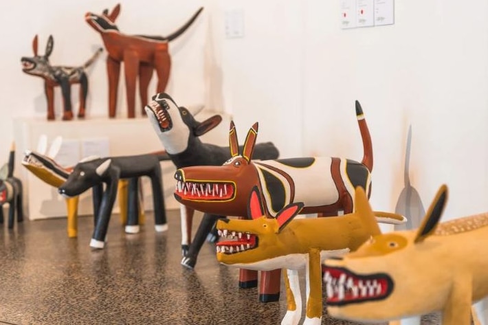 A collection of brightly coloured wooden carvings of dogs in an art gallery.