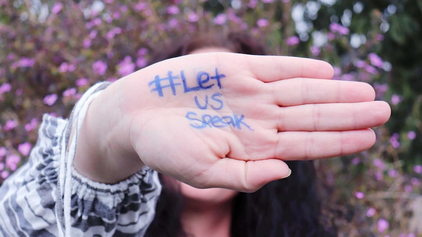 Woman holding up hand with Let us speak written on it.