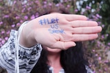 A woman holds up a hand with Let us speak written on it.