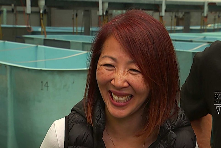 A fish farmer is smiling in front of tanks.