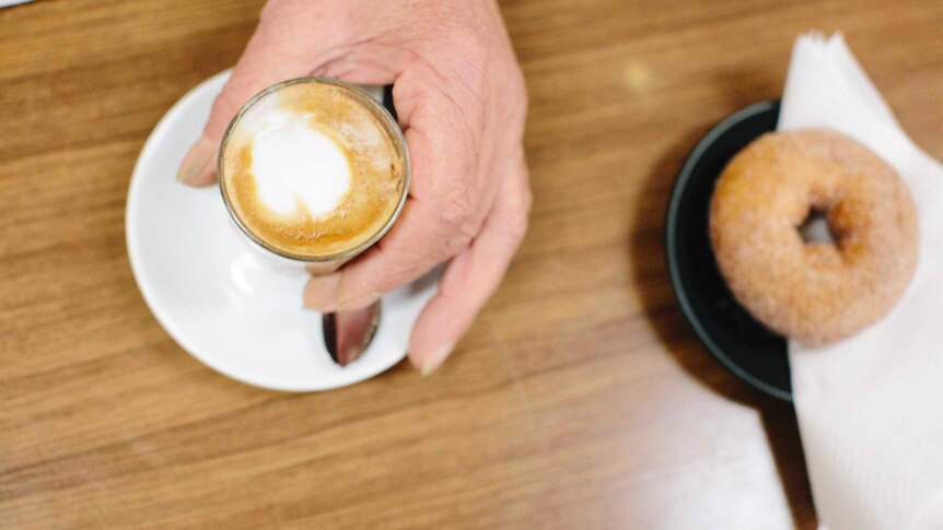 A customer picks up a long macchiato next to a doughnut