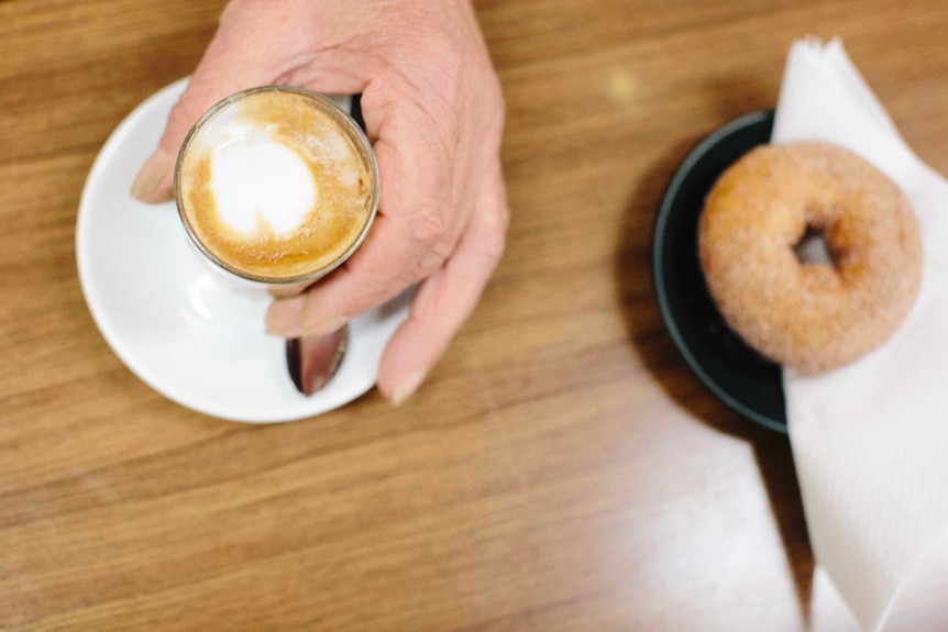 A customer picks up a long macchiato next to a doughnut