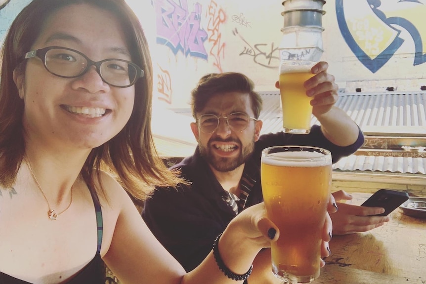 A woman and a man sitting outdoors in a pub holding beers.