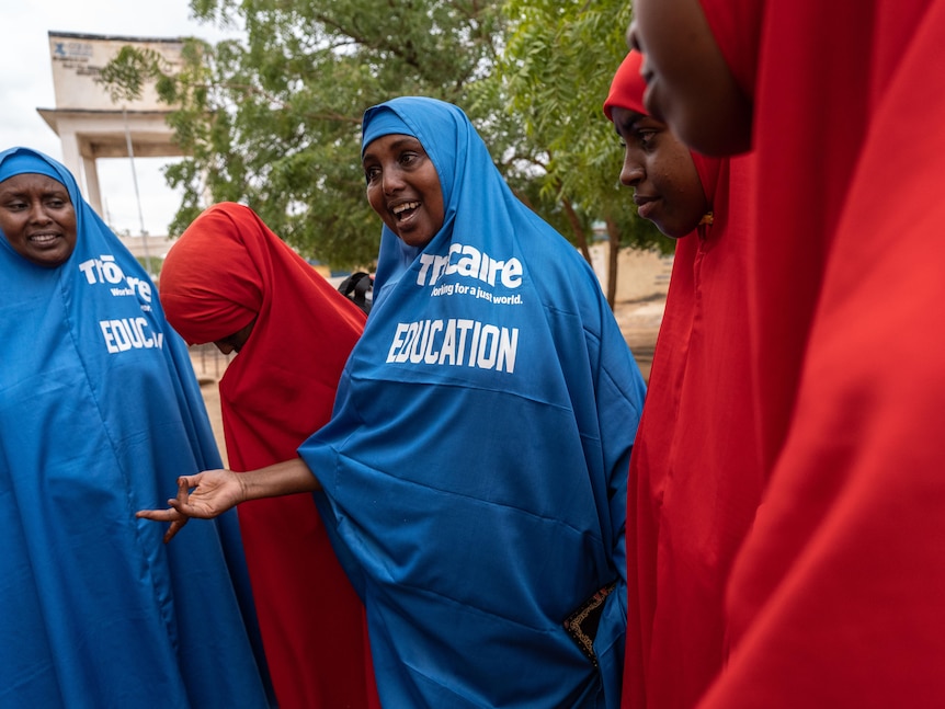 A woman wearing a blue head veil with the word EDUCATION on the chest gestures while talking to other women in red and blue