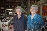 Elderly man in cowboy hat standing next to elderly lady on right in shop with shelves of leathers purses and bracelets.