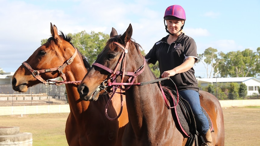 A woman riding a horse with another horse alongside