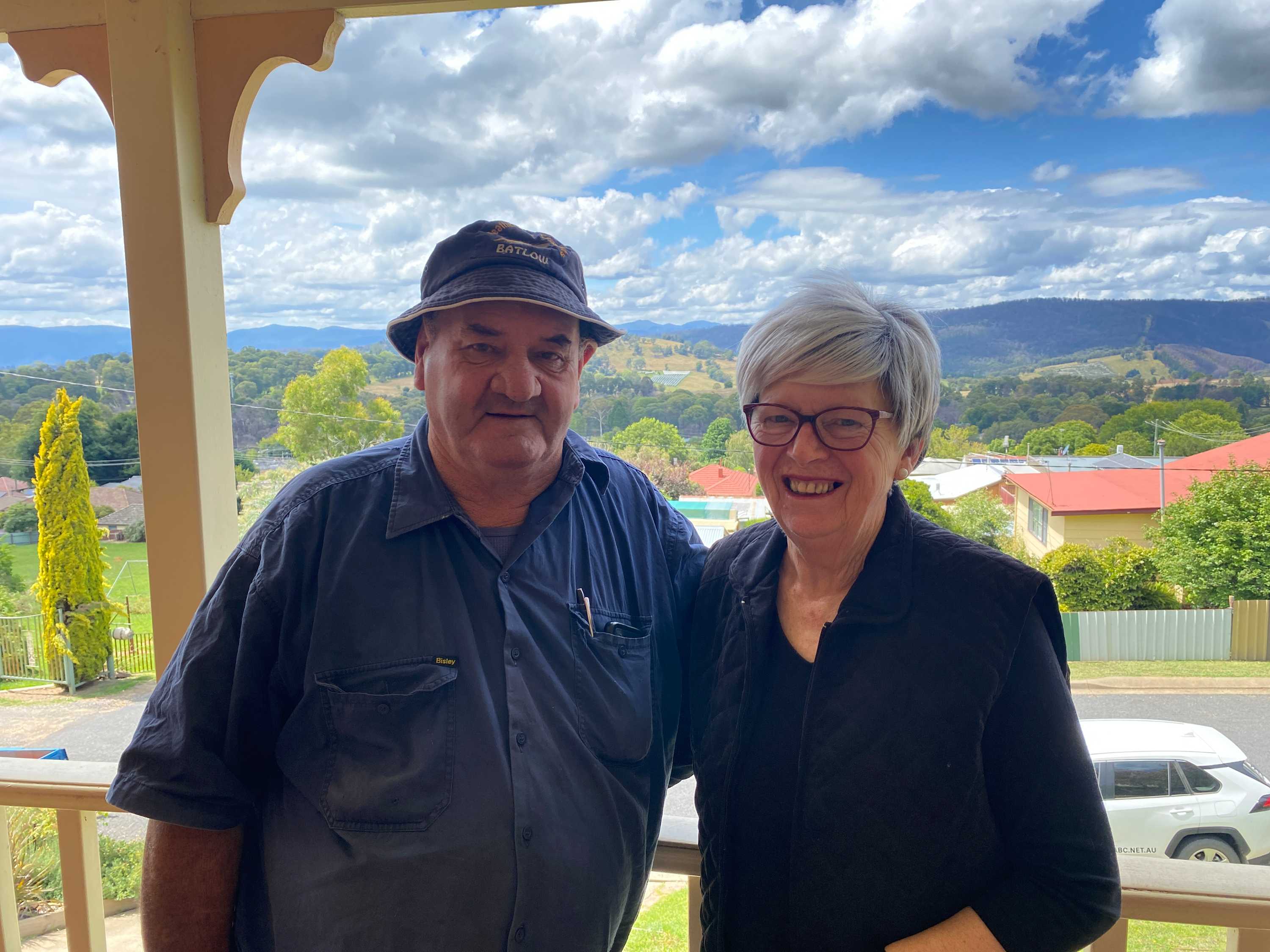 A man and a woman smiling with a hilly vista and blue and cloudy sky in the background.