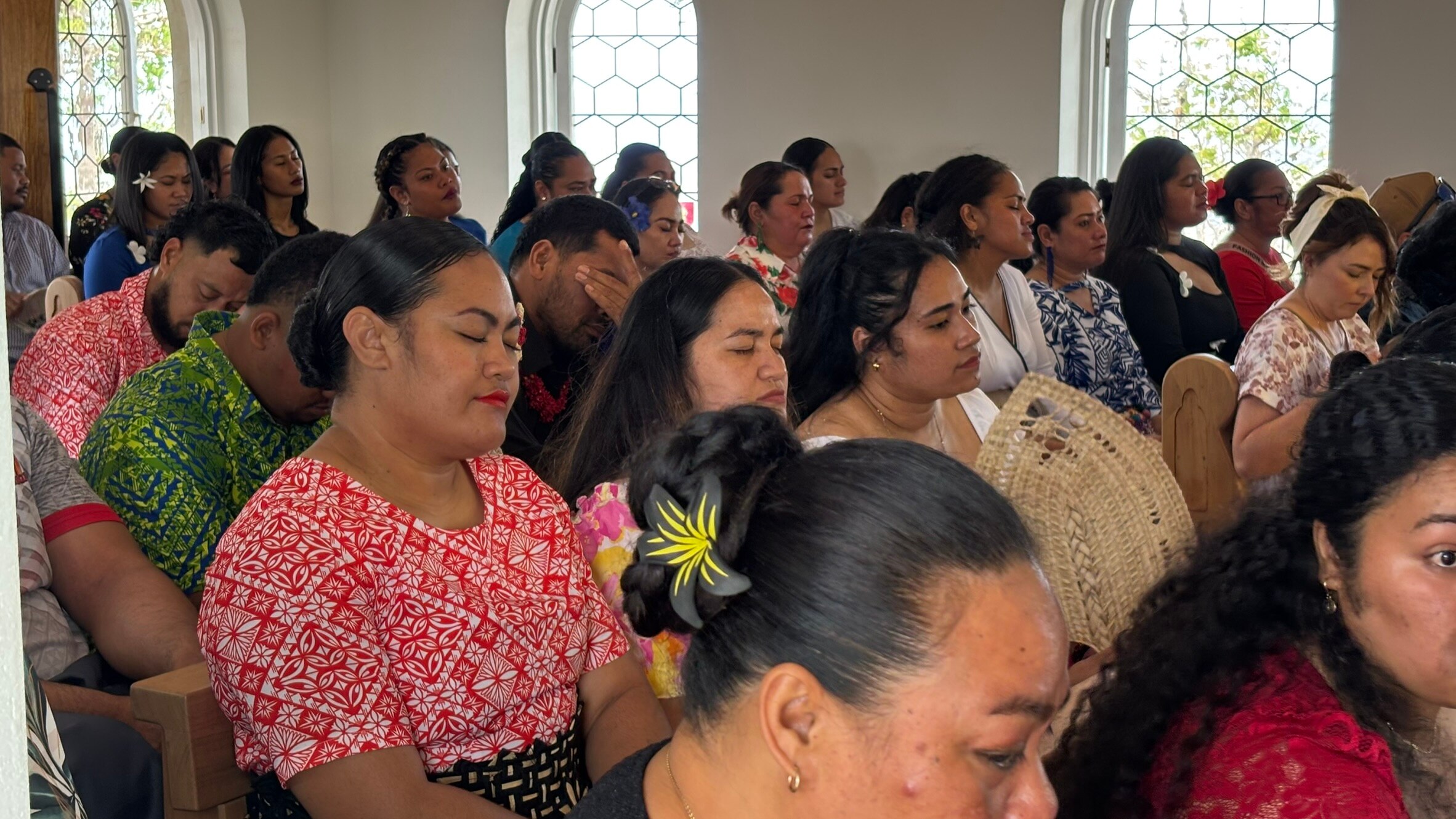 Hombres y mujeres se sientan muy juntos en bancos de madera en una pequeña capilla.