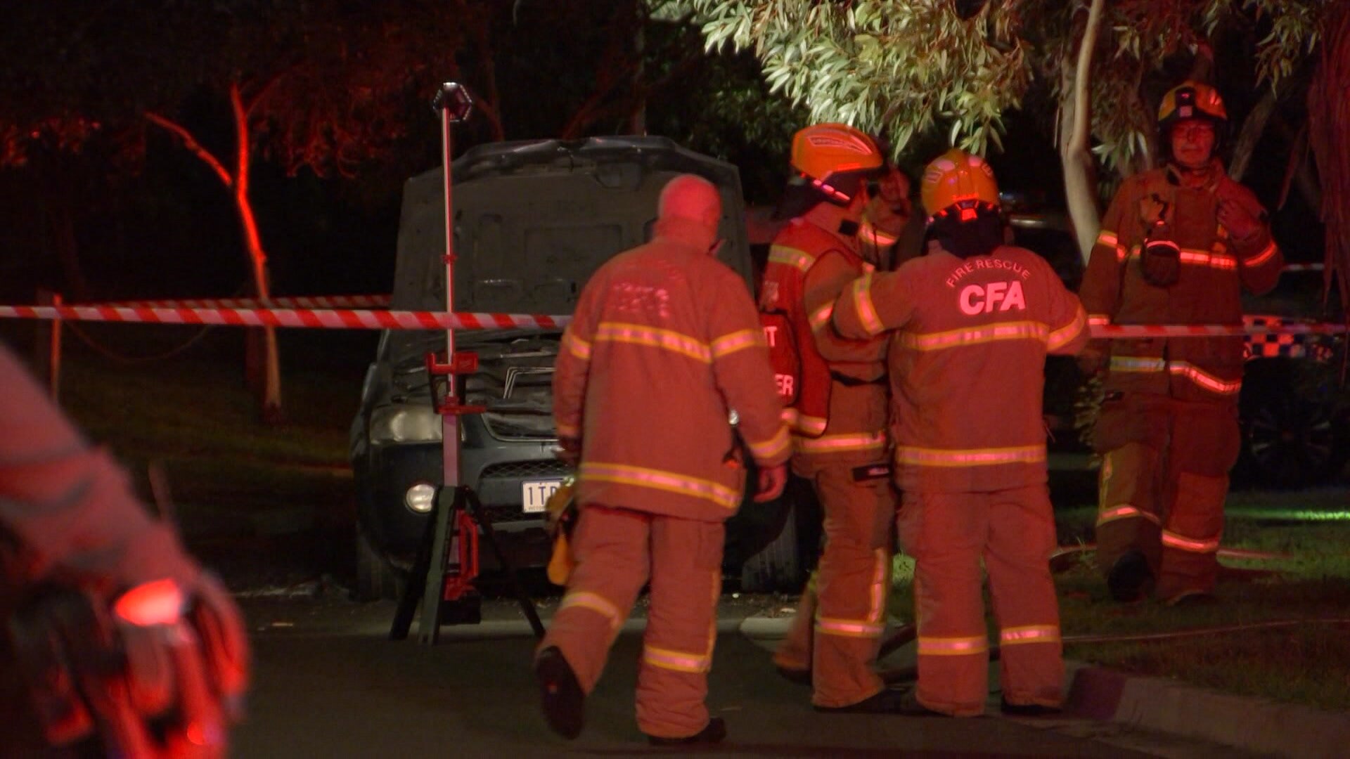 Emergency services crews surround a car at a crime scene at night.