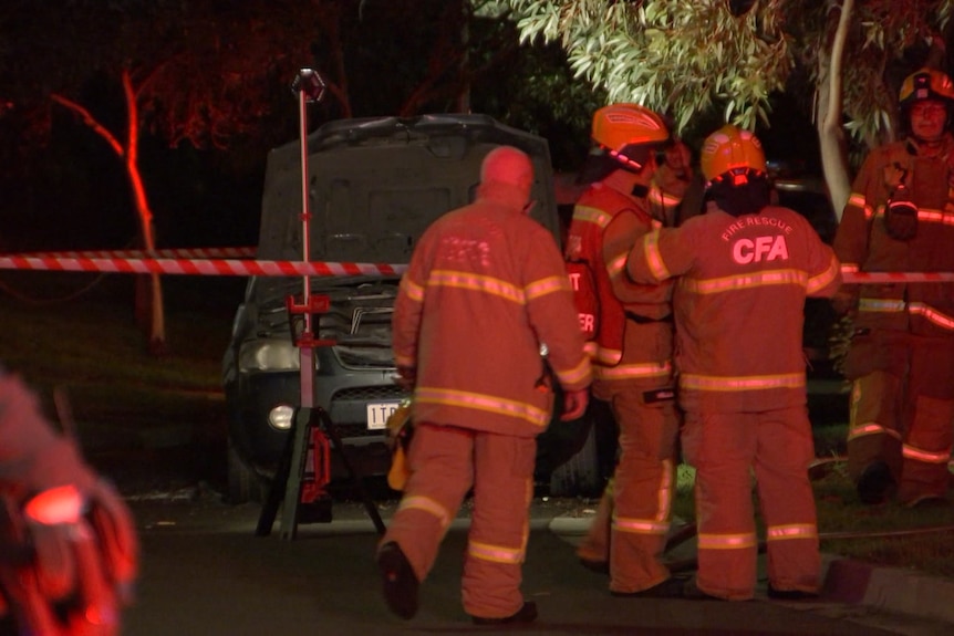 Emergency services crews surround a car at a crime scene at night.