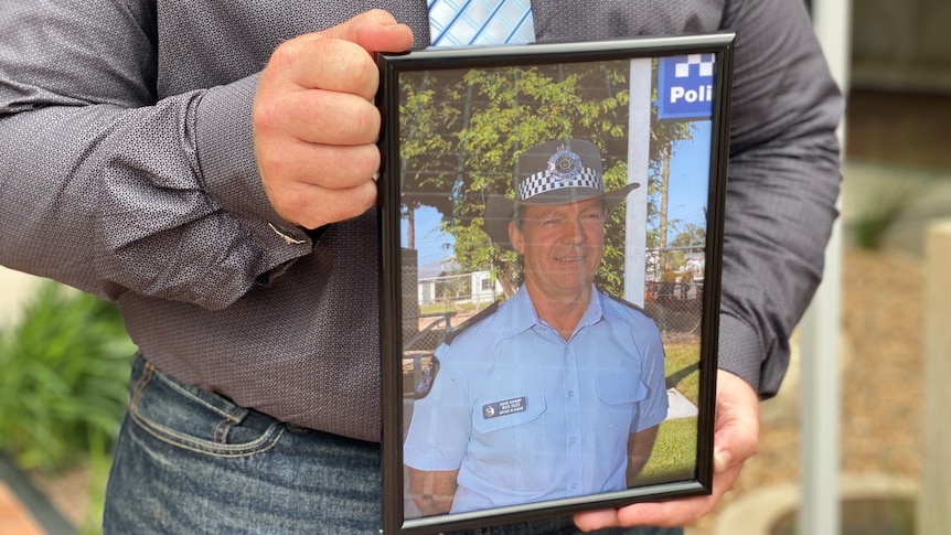 A framed photograph of a policeman in his uniform being held by a man's hands 