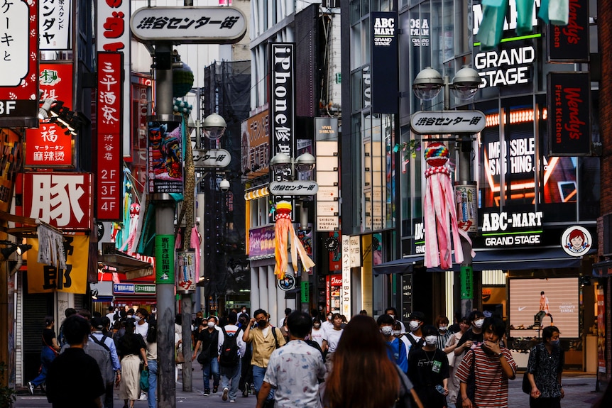 The very busy Shibuya district of Tokyo, crowds can be seen and everyone is outside and wearing masks.