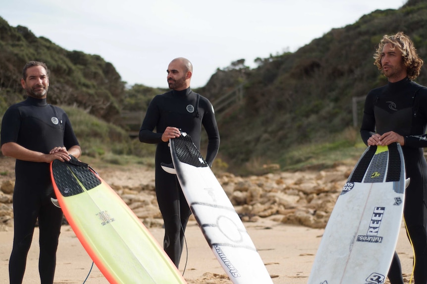 Anthony Hume, Cormach Evans and Jordie Campbell sand on Bells Beach wearing wetsuits and hold their surfboards.