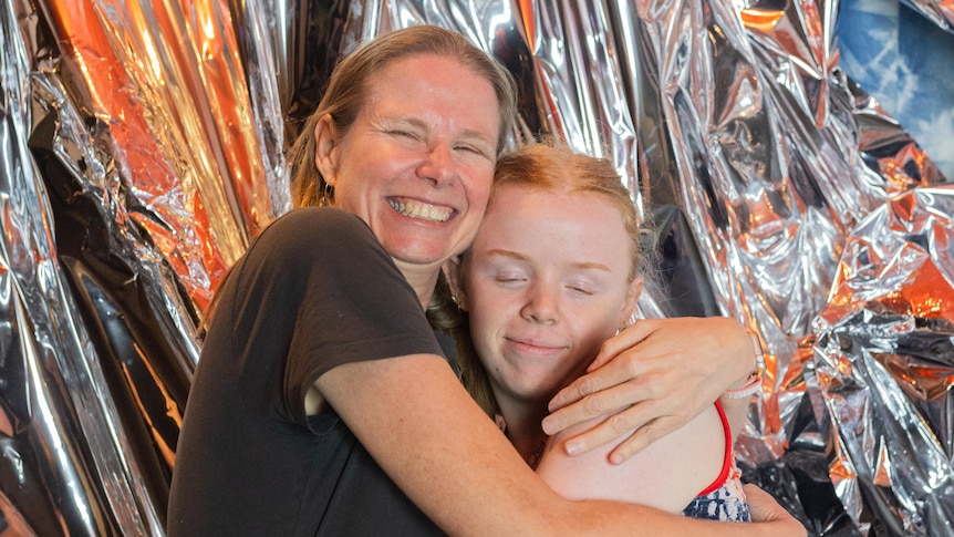 A woman smiling broadly while hugging her daughter, who has her eyes closed and is smiling and embracing her mum