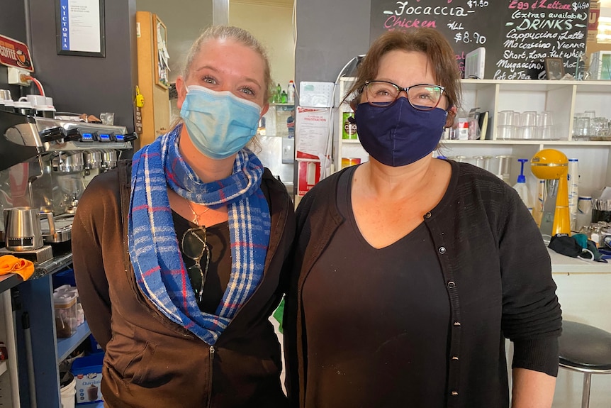 Two women wearing masks standing behind the counter at a cafe