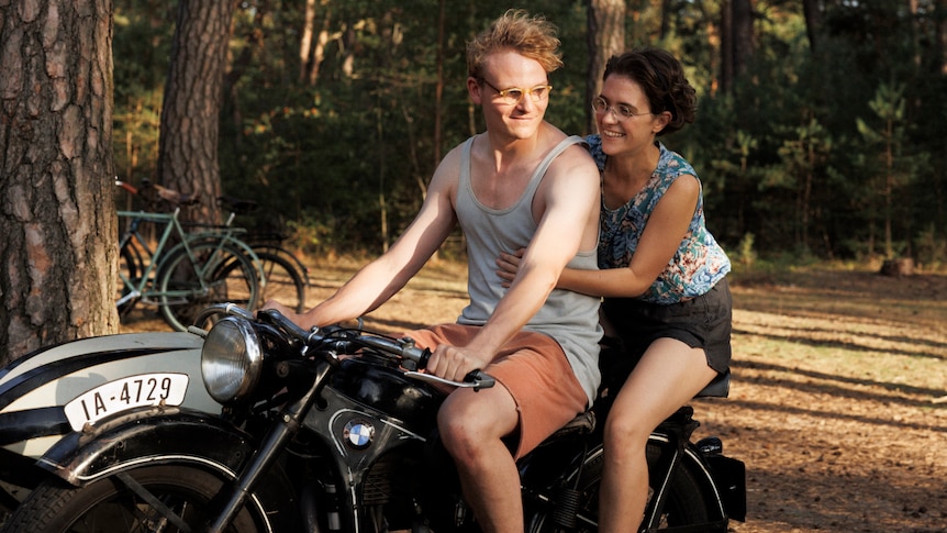 A film still of Johannes Hegemann on a 40s-style motorbike, with Liv Lisa Fries seated behind him.