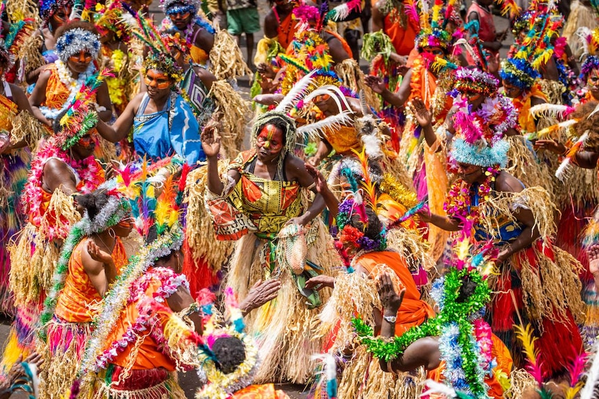 A large number of colourful women dance wearing grass skirts.