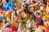 A large number of colourful women dance wearing grass skirts.
