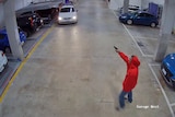 CCTV vision shows man dressed in red hoodie and jeans pointing a handgun at a white station wagon.
