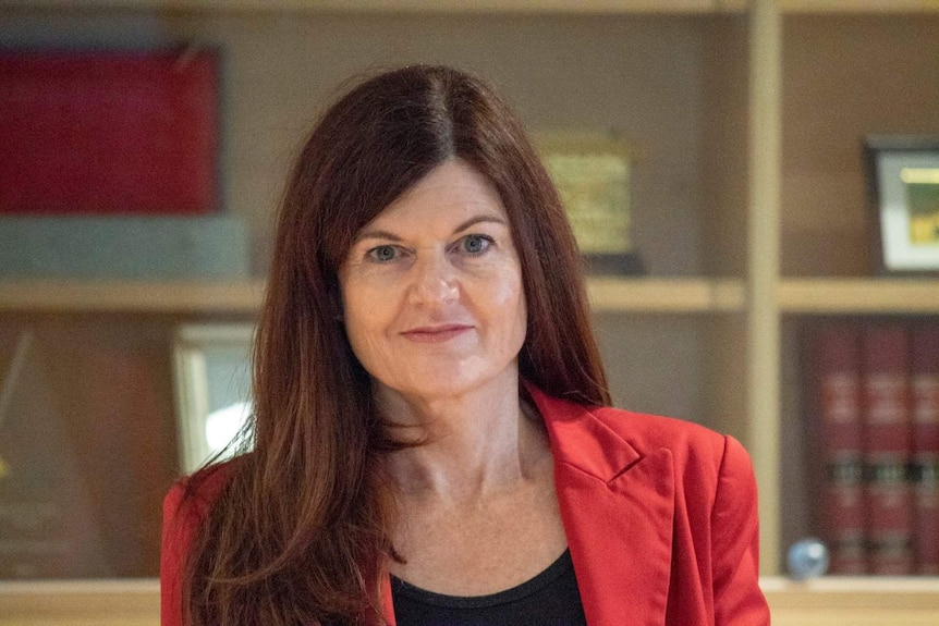 A woman stands in front of a book shelf and looks at the camera