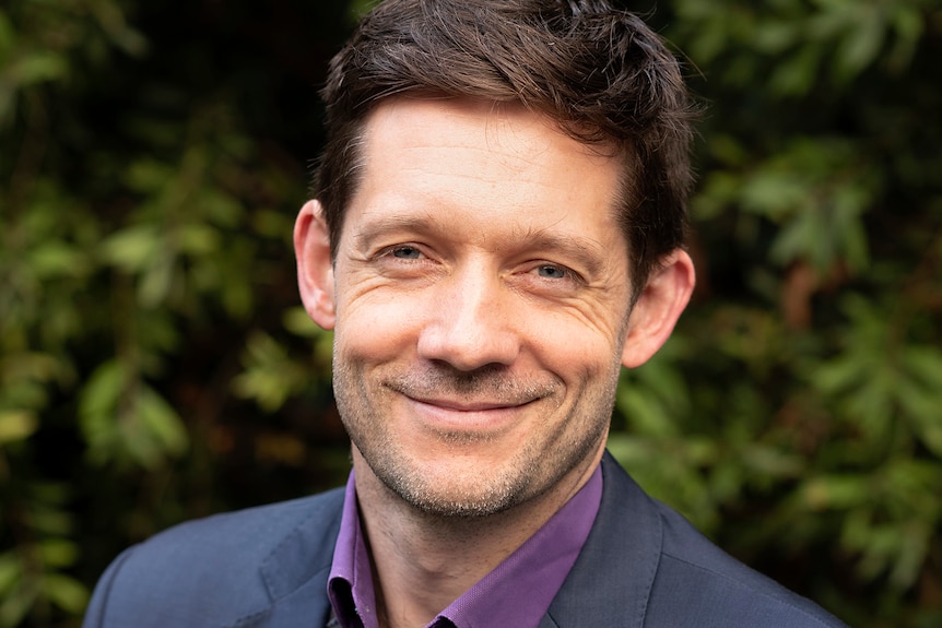 Man with suit jacket and brown hair smiles at camera.