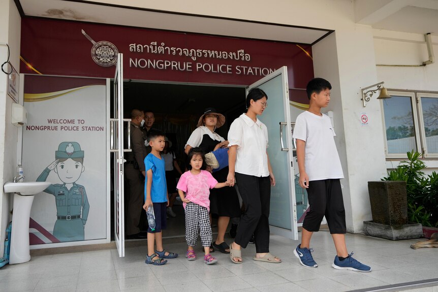A group of Chinese people, including a woman holding hand of a girl in pink shirt, walk out of a Thai police station.