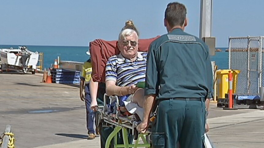 Paramedics wheel an elderly man on a stretcher along a jetty.