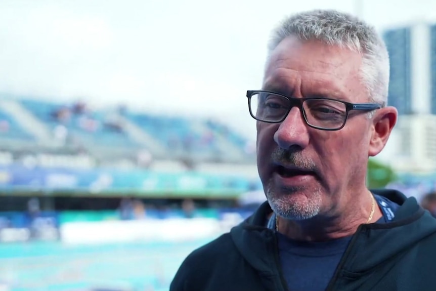 A man wearing glasses stands next to a swimming pool