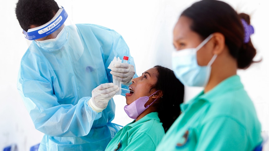 A medical worker wearing PPE takes a swab sample from a woman's mouth