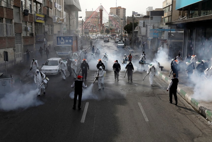 Firefighters disinfect a street in protective gear in Tehran.