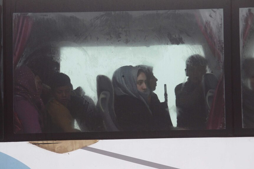 View of women and children sitting on a bus through a foggy window.