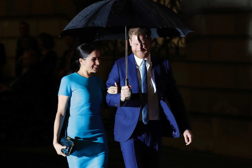 Britain's Prince Harry and Meghan walk together under an umbrella.