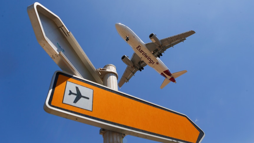 A plane flies past a sign pointing to an airport