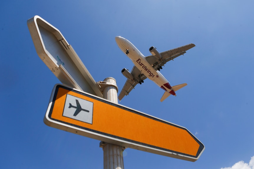 A plane flies past a sign pointing to an airport
