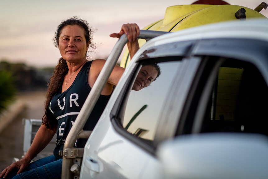 A woman sits on the back of a ute looking at the camera