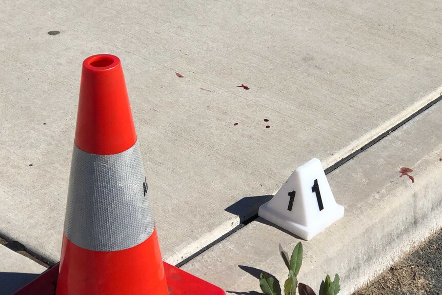 A close up of drops of blood on a concrete footpath, with a police sign with the number one on it and a red marker next to it.