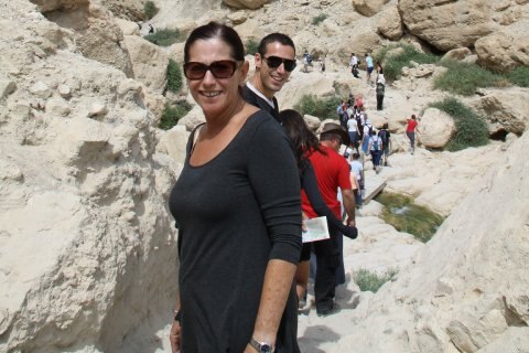 Woman wearing sunglasses smiles with long line of people on rocky track behind her