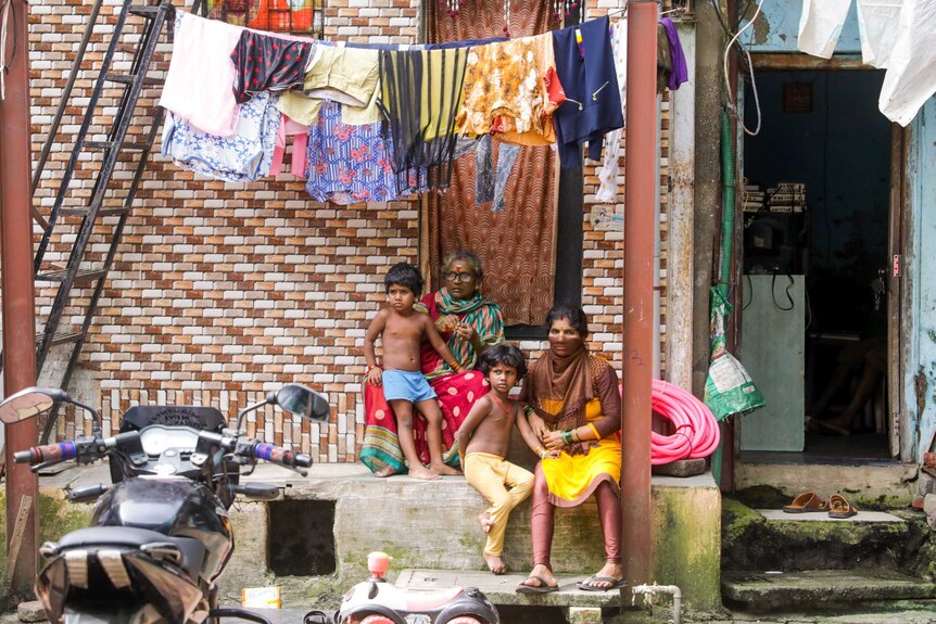 A grandmother, mother and two small children sit on a stoop under a line of washing